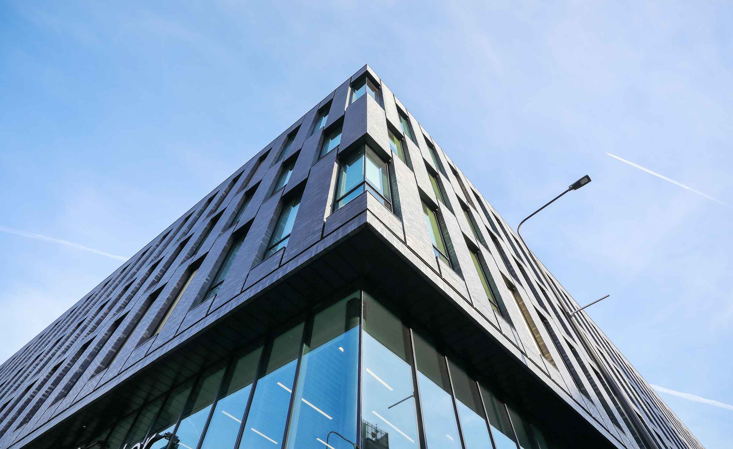 The corner of a modern educational building. The camera is angled to the sky which is blue and clear.