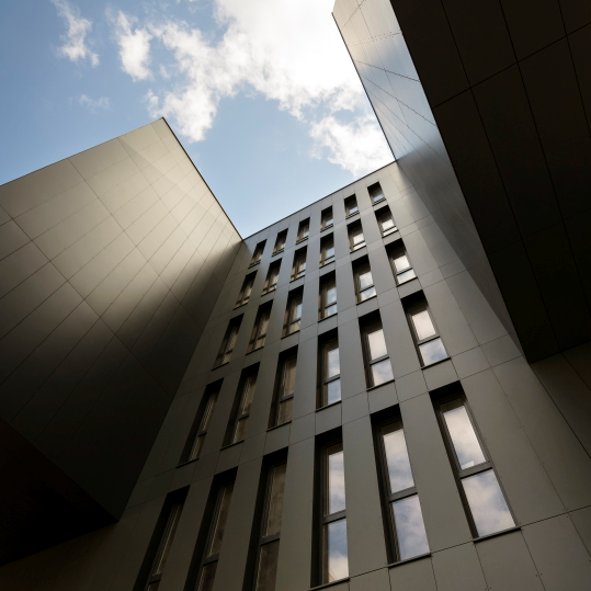 A tall building with slim, aluminium windows is taking up most of the image. We are looking upward toward a blue sky.